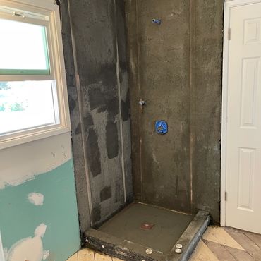 Shower construction in progress with cement base and plumbing.