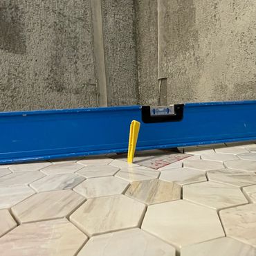 Yellow tile spacer on hexagonal marble tiles with blue level tool.
