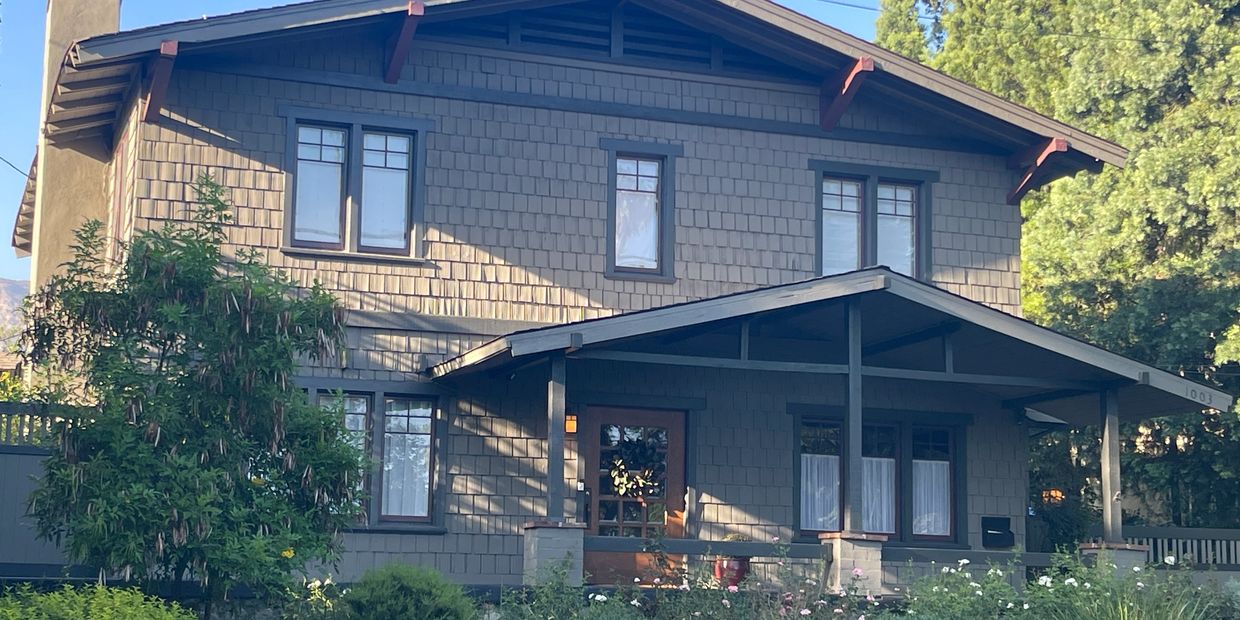 Large house with porch and greenery.