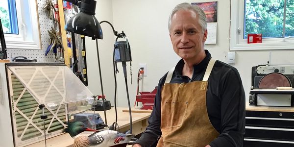 Man holding decorated wooden duck in workshop.