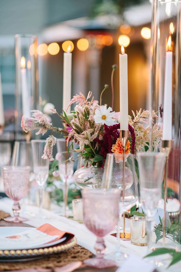 Elegant table setting with lit candles and floral centerpiece in soft lighting.