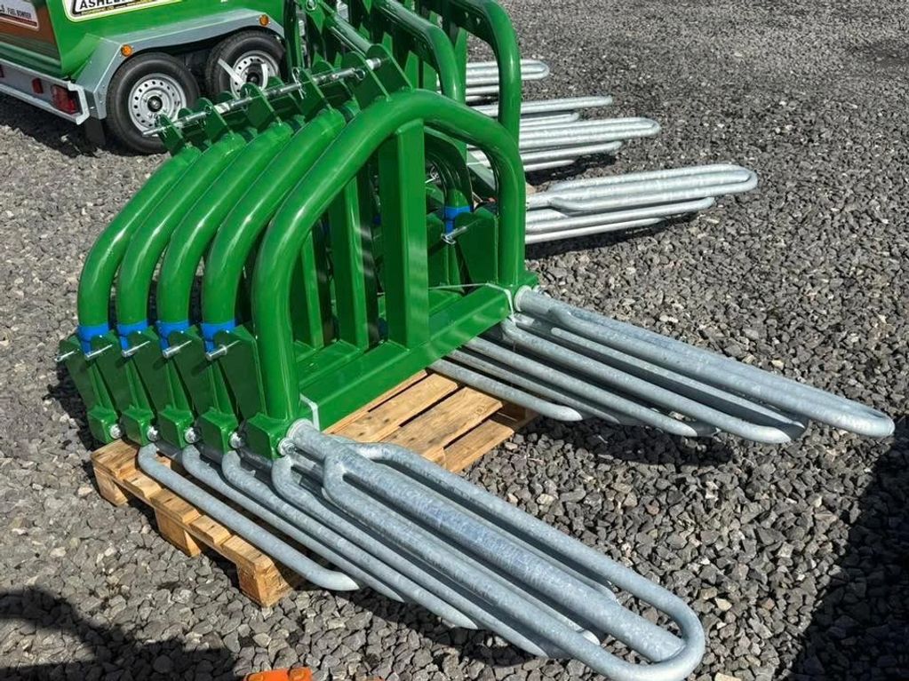 Green metal farming equipment attachments with prongs on a wooden pallet outdoors.