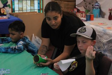 Woman helps two boys with a craft activity.