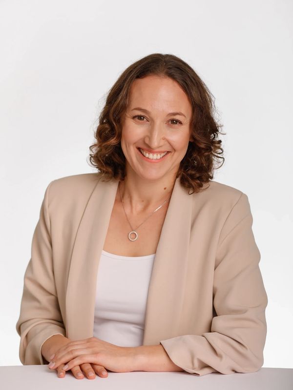 Smiling woman in beige blazer posing against a white background.