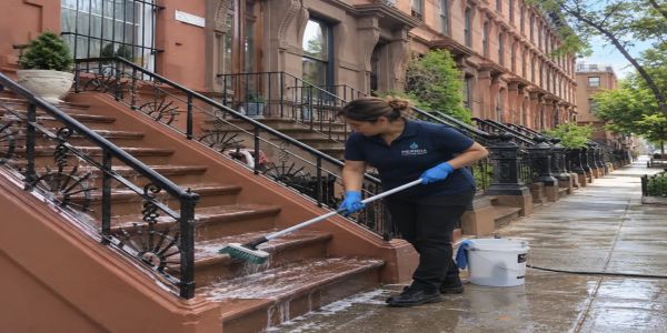 Person cleaning outdoor stairs with a brush and soap water.