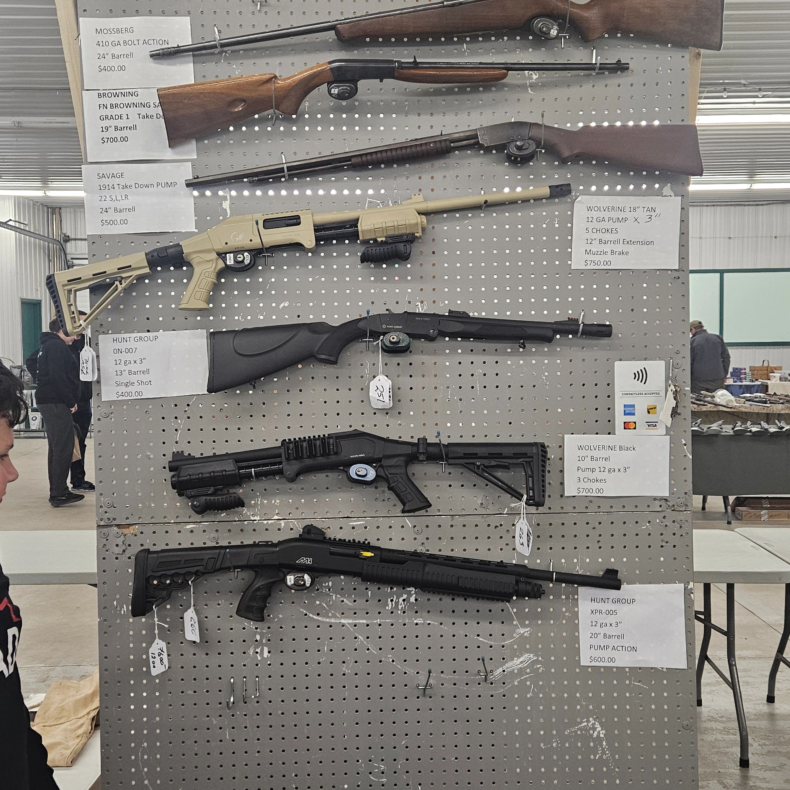 Various firearms displayed on a pegboard with price tags and descriptions.
