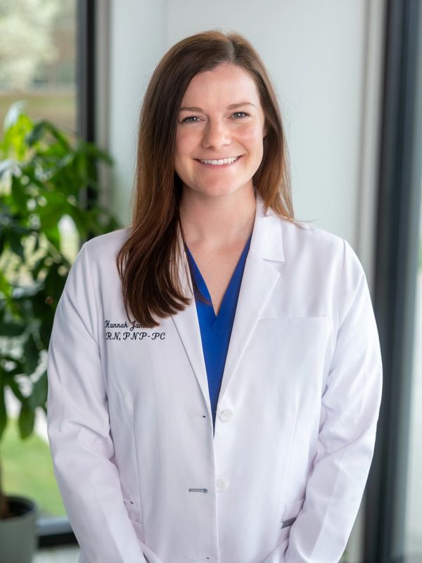 Smiling female nurse practitioner in white coat indoors.