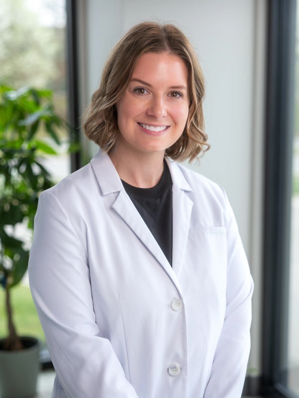 Smiling woman in a white lab coat standing indoors.
