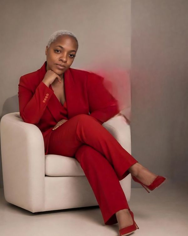 Confident woman in a red suit sitting on a white chair.