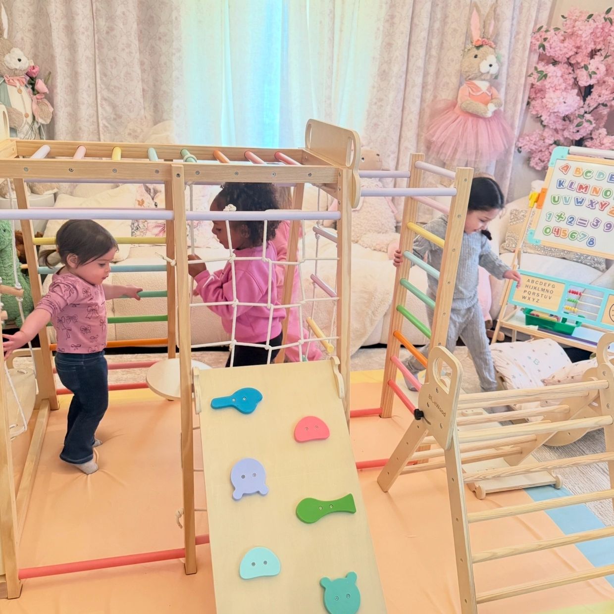Three children playing on a colorful indoor climbing structure in a cozy room.