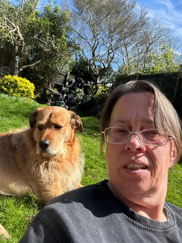 Person with glasses and a dog outside in a garden.