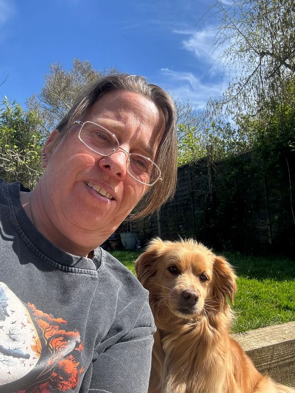 Person with glasses taking selfie with a golden dog outdoors.