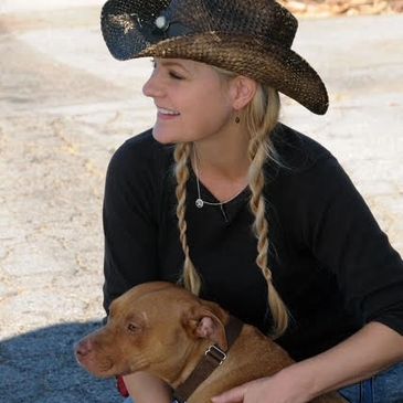Woman with braided hair and cowboy hat holding a brown dog.