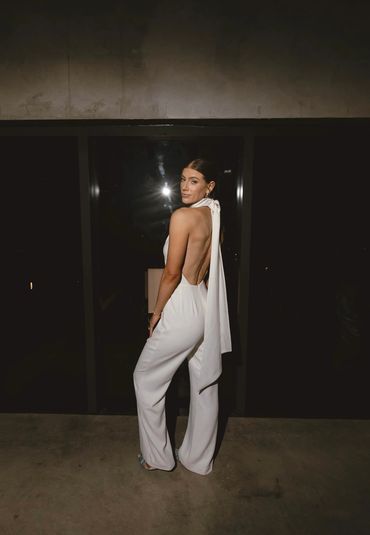 Woman in elegant white backless jumpsuit posing.