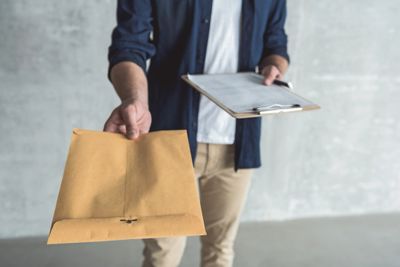 Person holding a clipboard and offering a large brown envelope.