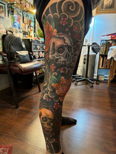 Full leg tattoo featuring skulls, flowers, and swirling patterns in vibrant colors.