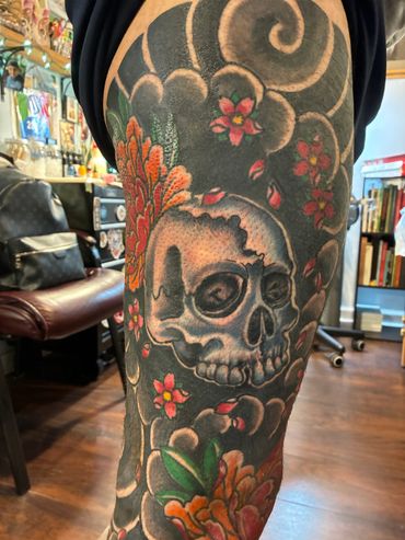 Colorful skull tattoo with flowers and swirling patterns on leg.