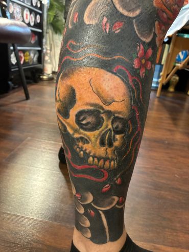 A detailed skull tattoo with red accents on a person's leg.