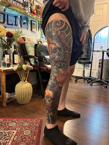 Colorful skull and floral full leg tattoo on a person's leg.