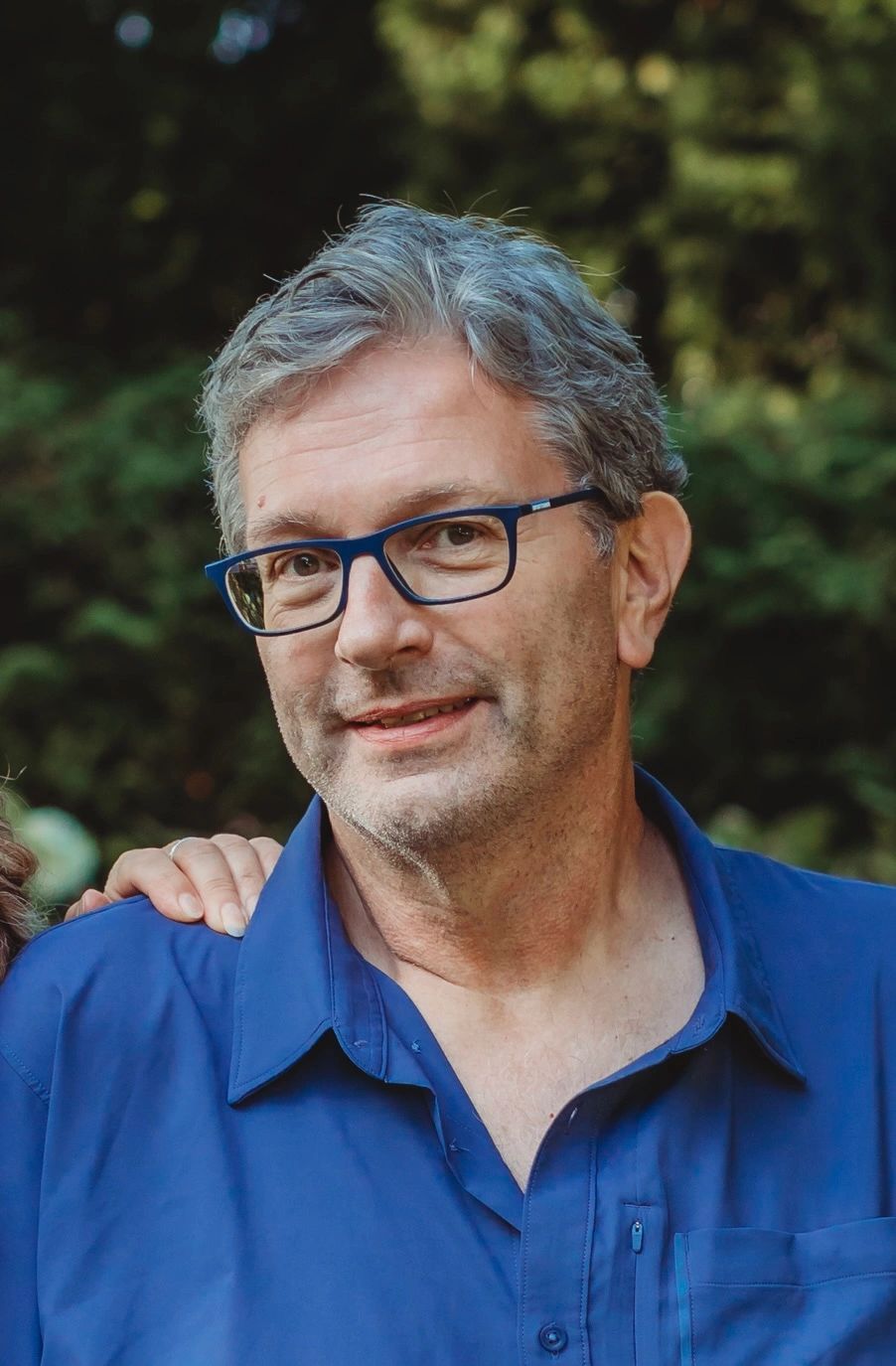 Middle-aged man with gray hair and glasses smiling outdoors.