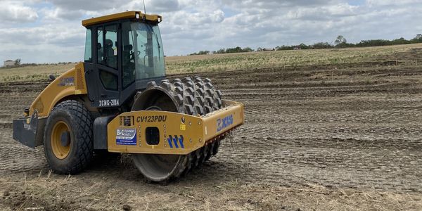Heavy roller compactor working on a dirt field.