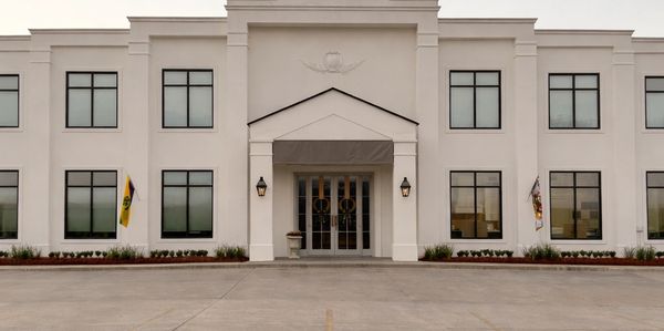 Front view of a modern white government or institutional building with symmetrical windows and flags.