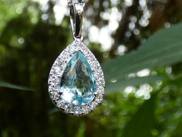 Close-up of a teardrop-shaped pendant with a blue gem and diamond border.