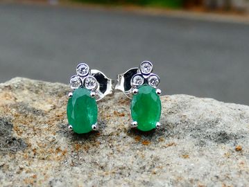 Elegant emerald and diamond stud earrings on a rock.