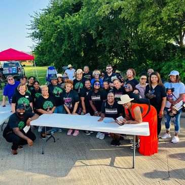 Group of people gathered outdoors around a table, smiling and posing for a photo.