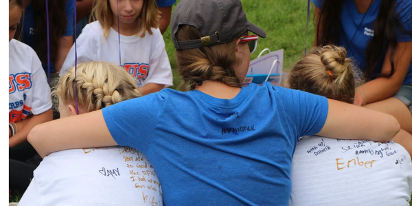 Three girls sitting closely, wearing signed shirts, showing friendship and support.