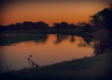 A serene lake at sunset with trees reflected in the water.