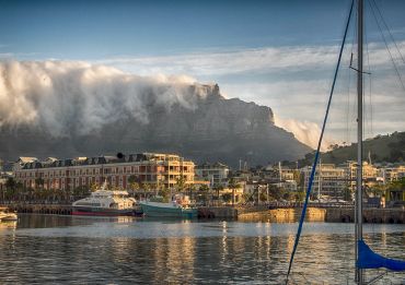 A waterfront city with boats and mist rolling over a mountain.