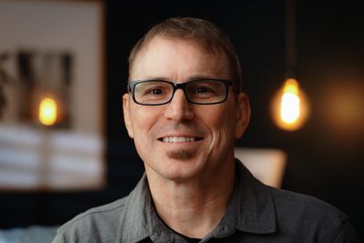 Smiling man wearing glasses in a warmly lit room.