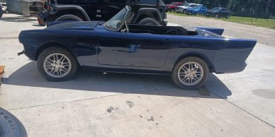 Side profile view of a dark blue 1962 Sunbeam Alpine classic roadster parked outdoors in front of a 