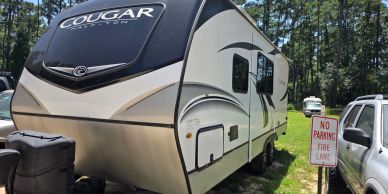 Front-three-quarter view of a white and black 2022 Keystone Cougar fifth-wheel RV trailer parked on 