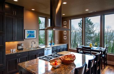 Gourmet kitchen with charcoal cabinetry, expansive chef’s island, granite countertops, and sun-fille