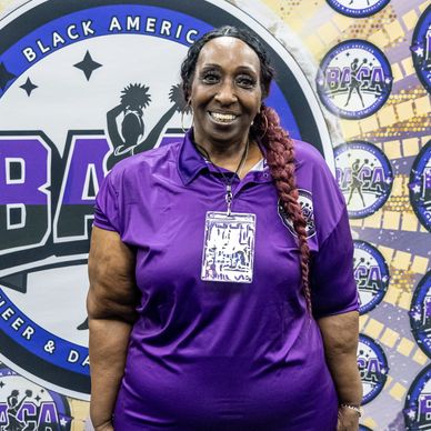 Woman in purple shirt smiling at a Black American Cheer &amp; Dance event.