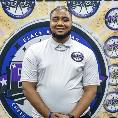 Man smiling in front of Black Asian Cheer and Dance Association backdrop.