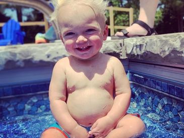 A happy toddler sitting in a small pool on a sunny day.