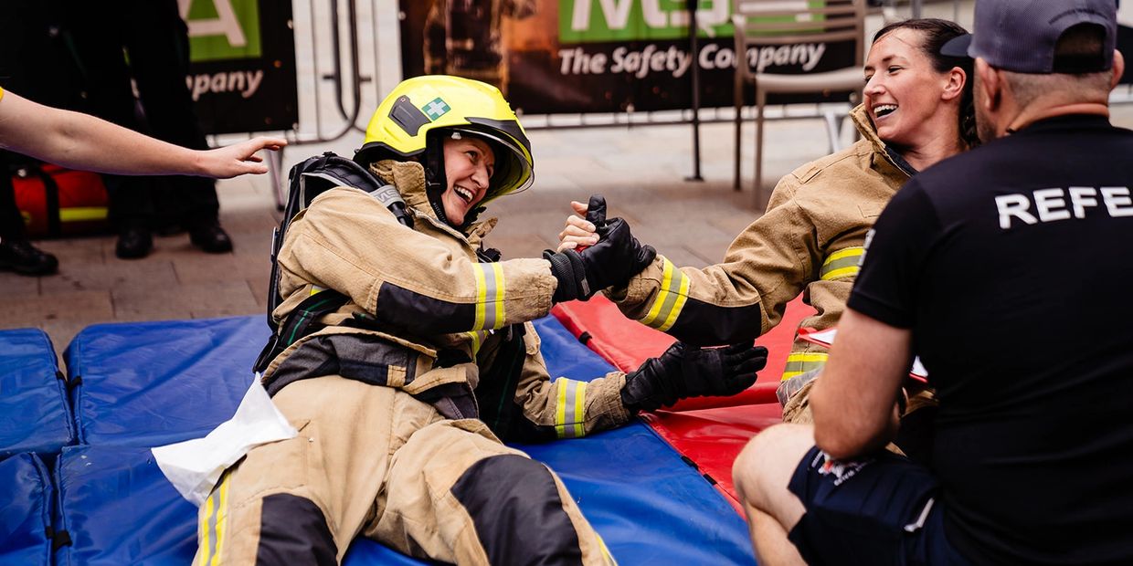 Two firefighters in gear share a joyful handshake on mats during a competition or training.
