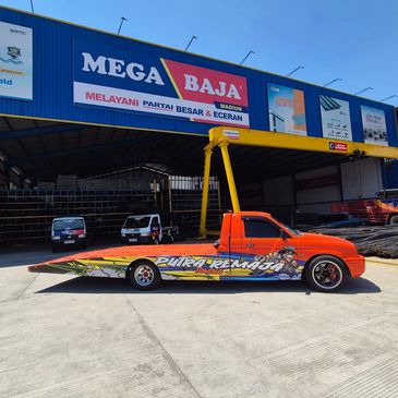 Bright orange flatbed truck with colorful graffiti parked outside a steel supplier warehouse.