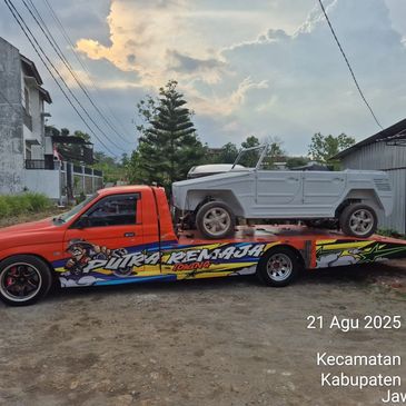 A colorful tow truck carrying a white convertible vehicle under a cloudy sky.