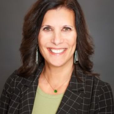 Smiling woman with dark hair wearing a checkered blazer and green top.