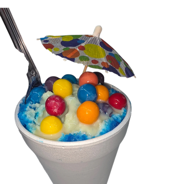 Colorful shaved ice topped with candy and a decorative umbrella in a white cup.