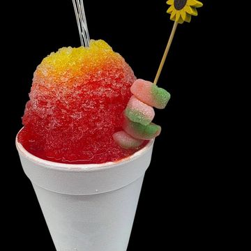 Colorful shaved ice in a white cup with gummy candy and sunflower pick.