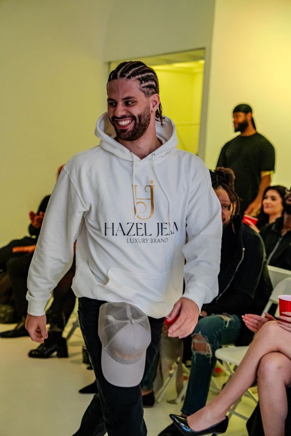Smiling man in a white hoodie walking past seated people at an indoor event.
