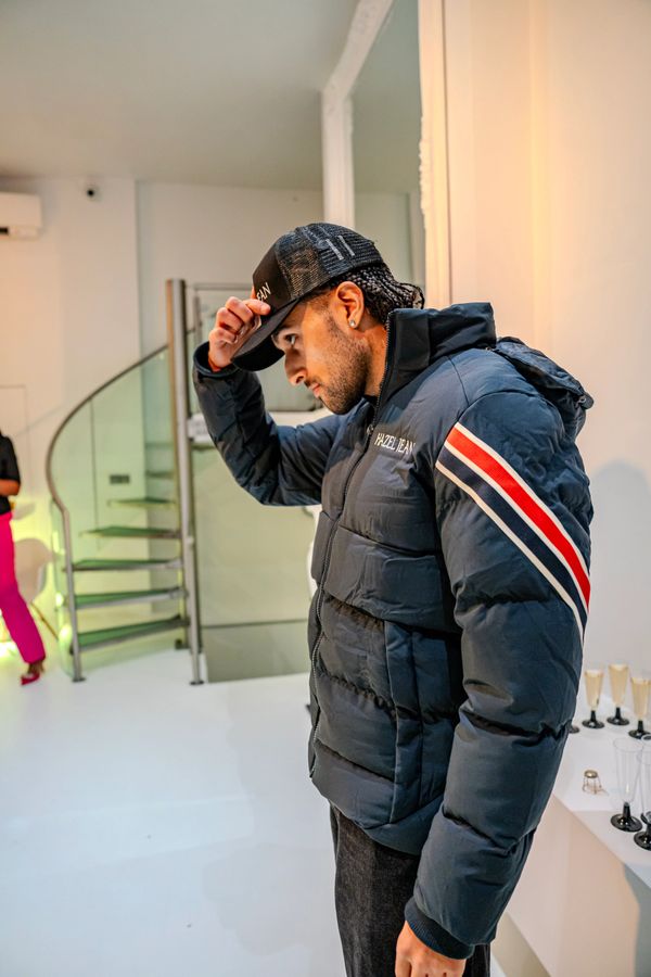 Man in a puffer jacket and cap adjusts his hat indoors.