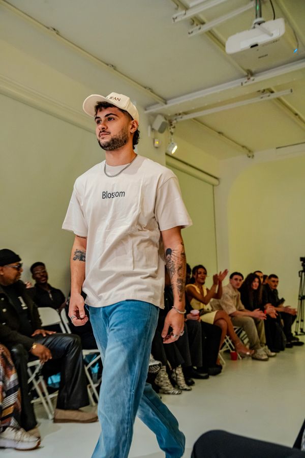 Man in casual attire walking on a runway with audience clapping.