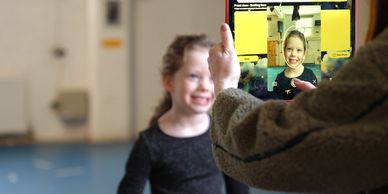 A child smiling while being captured on a tablet held by an adult.
