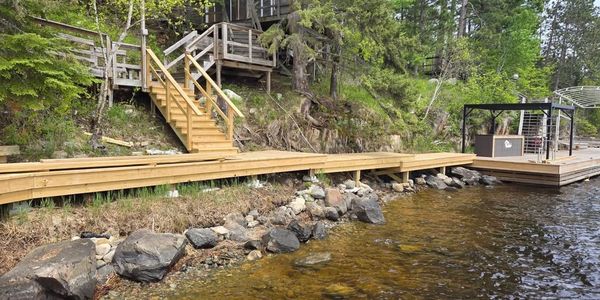 Wooden dock and stairs leading to a cabin by a lakeside surrounded by trees.